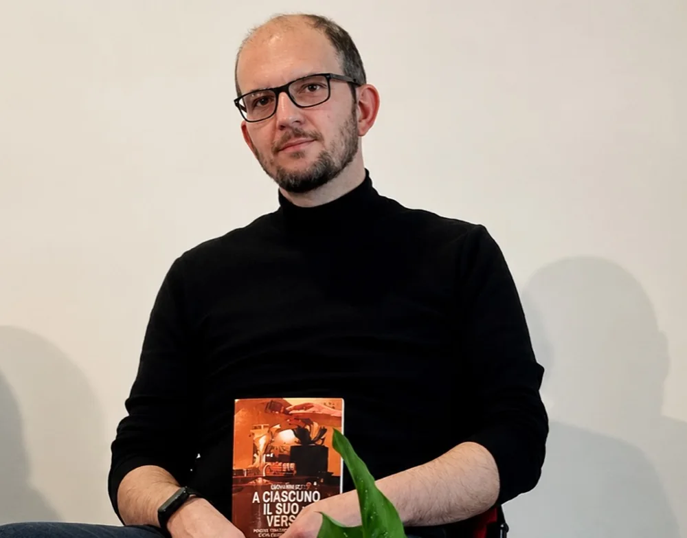 Max Rizzo seduto con in mano la raccolta A Ciascuno il Suo Verso